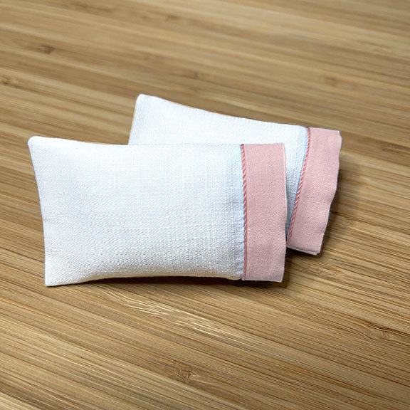 Two white cotton dollhouse miniature pillowcases with pink trim 1:12 scale, laid flat on a wooden surface
